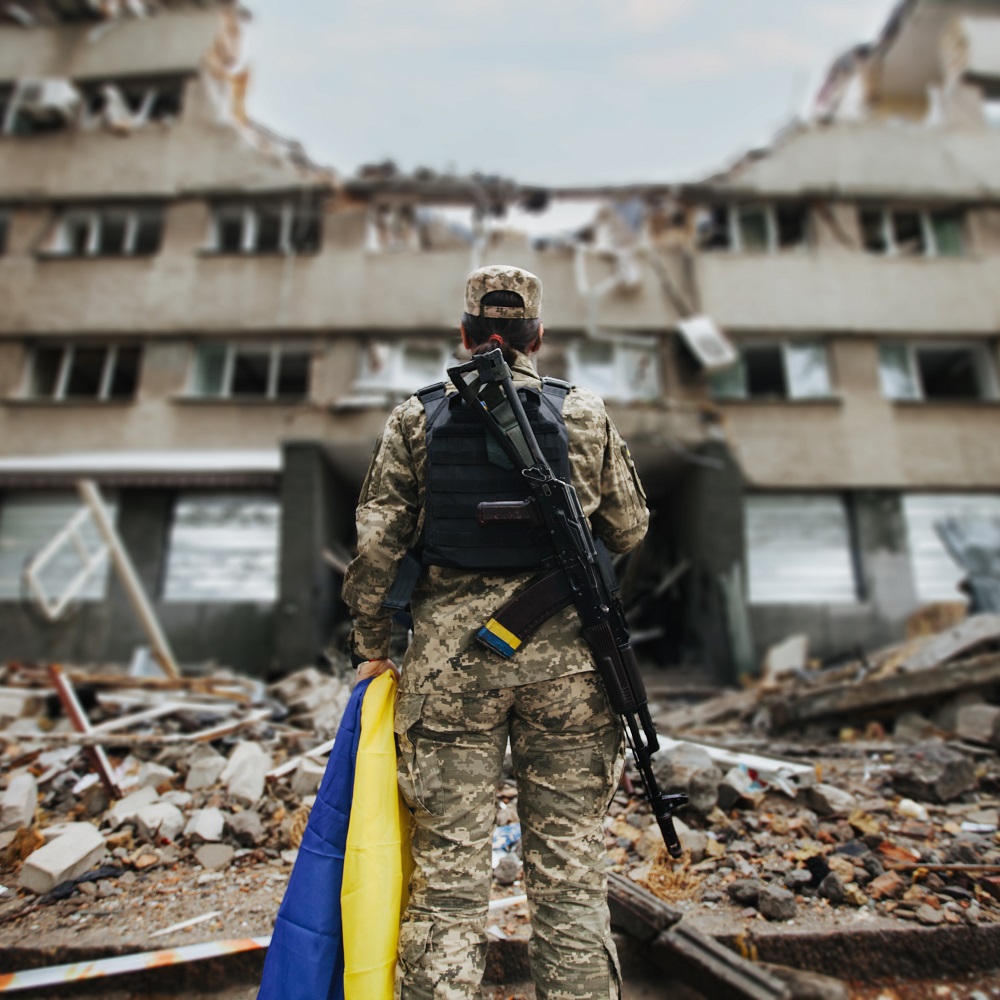 Ukrainian military woman with Ukrainian flag in her hands on the background of an exploded house					